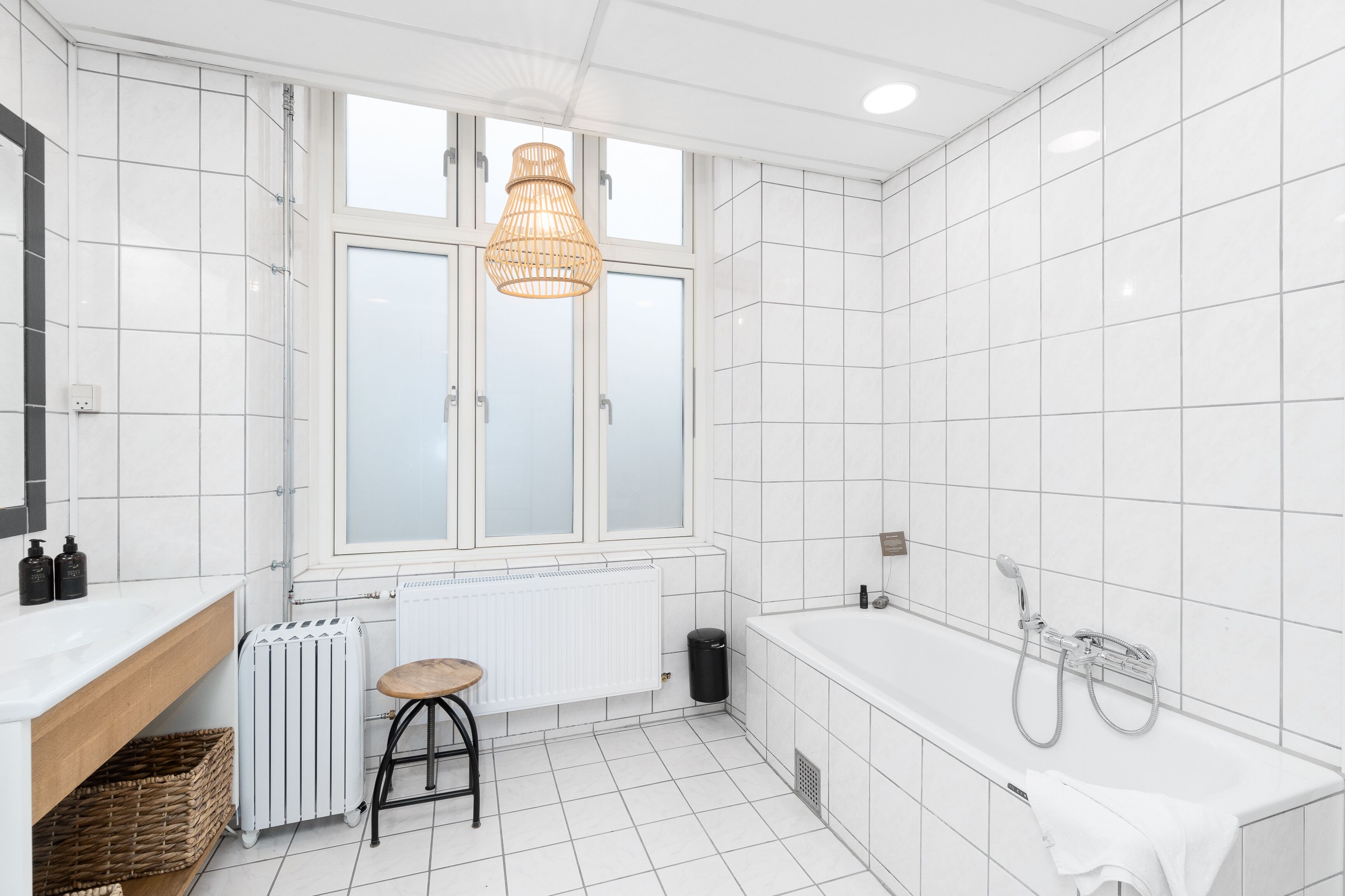 Un baño moderno con un ventanal grande, una bañera, un radiador y un taburete.