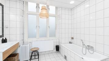 Un baño moderno con un ventanal grande, una bañera, un radiador y un taburete.