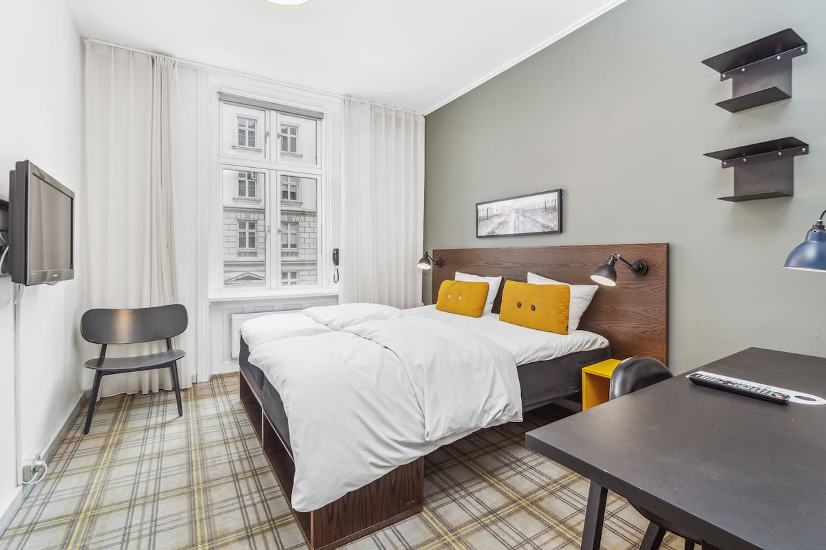 A modern hotel room with a large bed, a desk, a chair, and a TV.