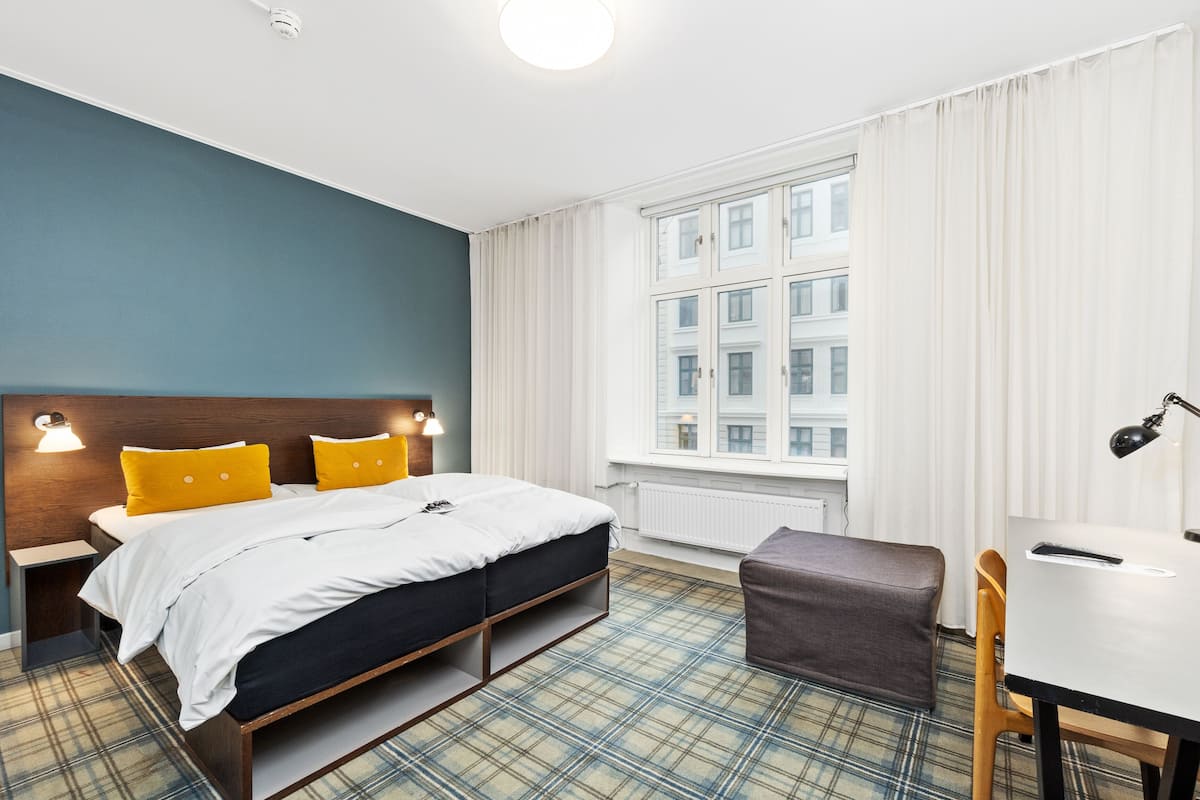 A hotel room with a bed, bedside tables, a desk, and a chair.