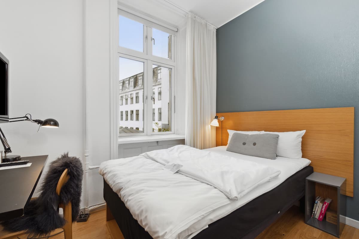 A neatly made bed with white linens, a wooden headboard, and a bedside lamp.