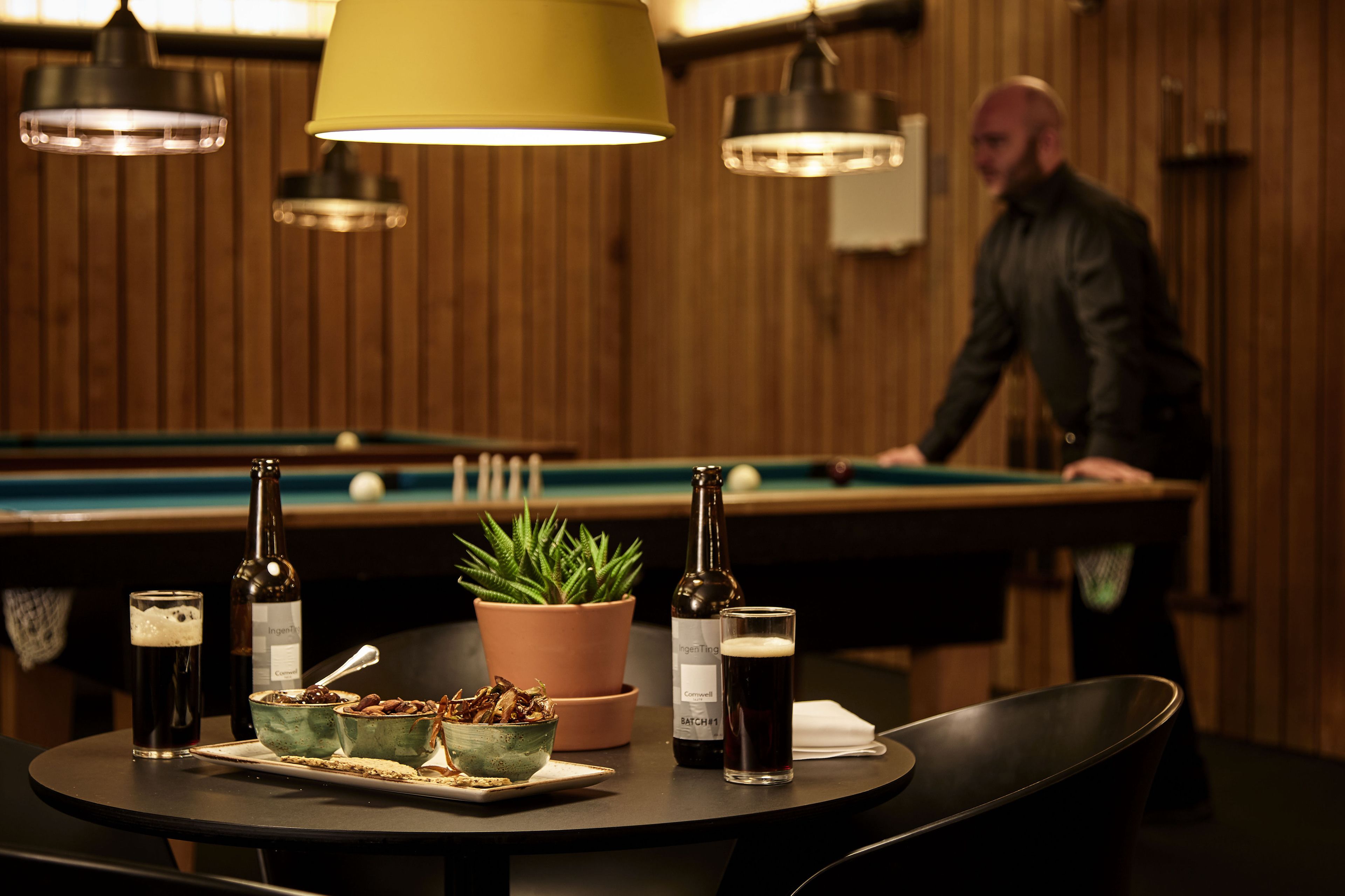 A pool table with a bottle of beer and a glass of beer on a table.