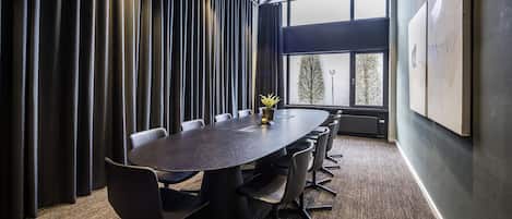 Une salle de conférence dotée d’une grande table ovale, de chaises noires, d’une plante en pot et offrant une vue sur l’extérieur grâce à une grande fenêtre.