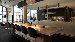 Un espace bar moderne avec un long comptoir, des tabourets de bar noirs et des luminaires sphériques suspendus.