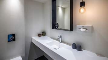 Ett modernt badrum med en vit tvättställ, en spegel, en handduksdispenser och en lampa.