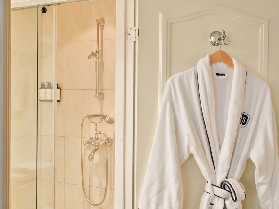 A bathroom with a glass shower enclosure, a white robe hanging on a door, and a towel rack.