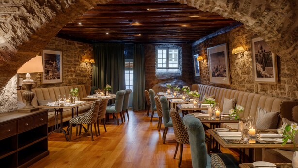 A cozy, rustic dining area with wooden beams, stone walls, and a vaulted ceiling. Tables are set with candles and flowers, and there are cushioned seating areas. - Schlössle Hotel - Small Luxury Hotels of the World (Tallinn)