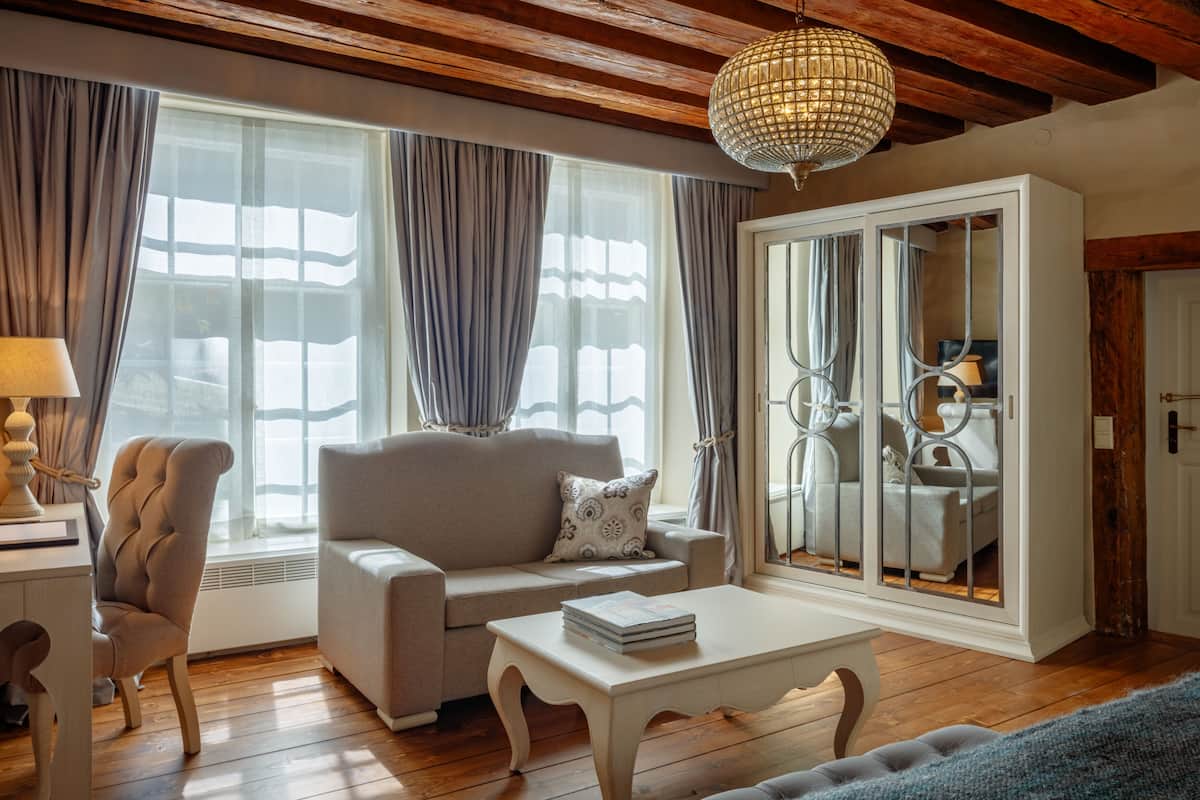 A living room with a sofa, a coffee table, a lamp, and a large window with curtains.