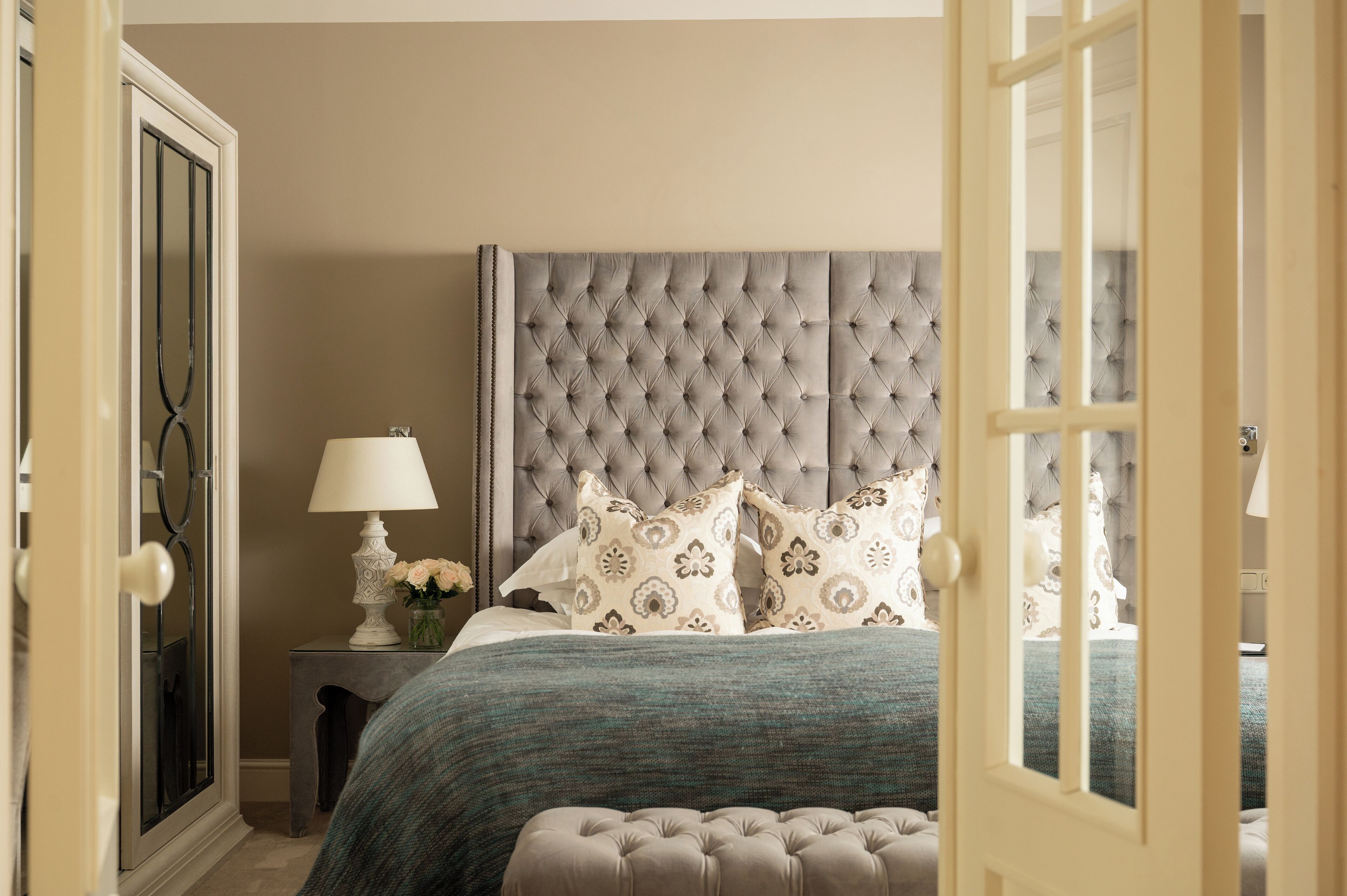 A bedroom with a tufted headboard, a bedside table with a lamp, and a bed with patterned pillows.