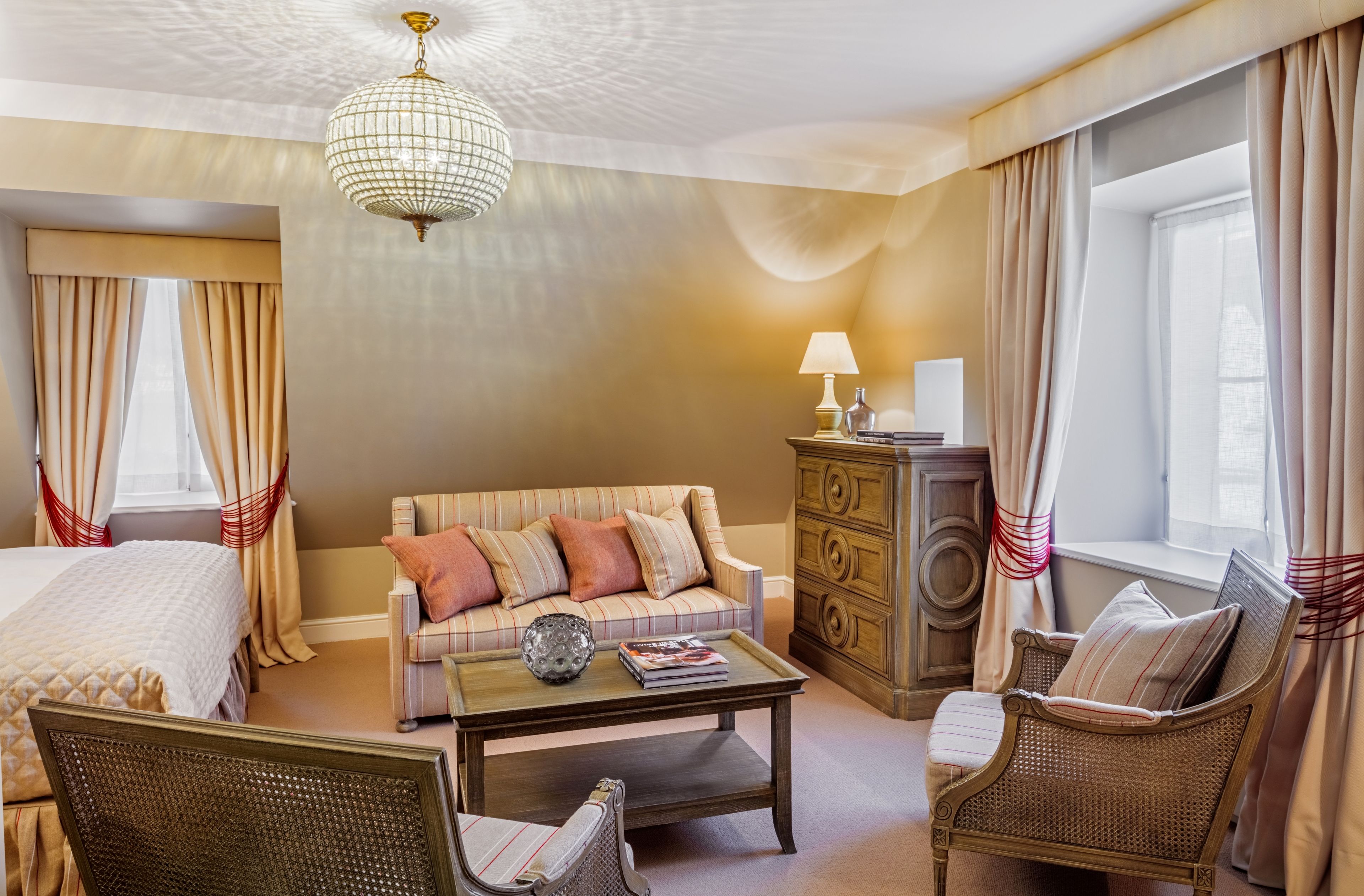 Habitación de hotel con cama, sofá, mesa de centro, sillón, cómoda y candelabro.