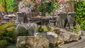 An outdoor dining area with wicker furniture, a stone fountain, and lush greenery. - Schlössle Hotel - Small Luxury Hotels of the World (Tallinn)