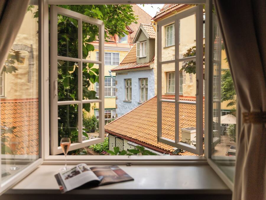 Une fenêtre donnant sur une cour, une table avec un verre de vin et un magazine posé sur le rebord de la fenêtre.