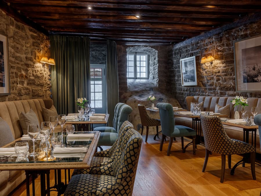 A cozy dining area with stone walls, wooden ceiling beams, and a mix of upholstered and patterned chairs.