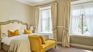 A bedroom with a bed, a yellow sofa, and two windows with curtains.