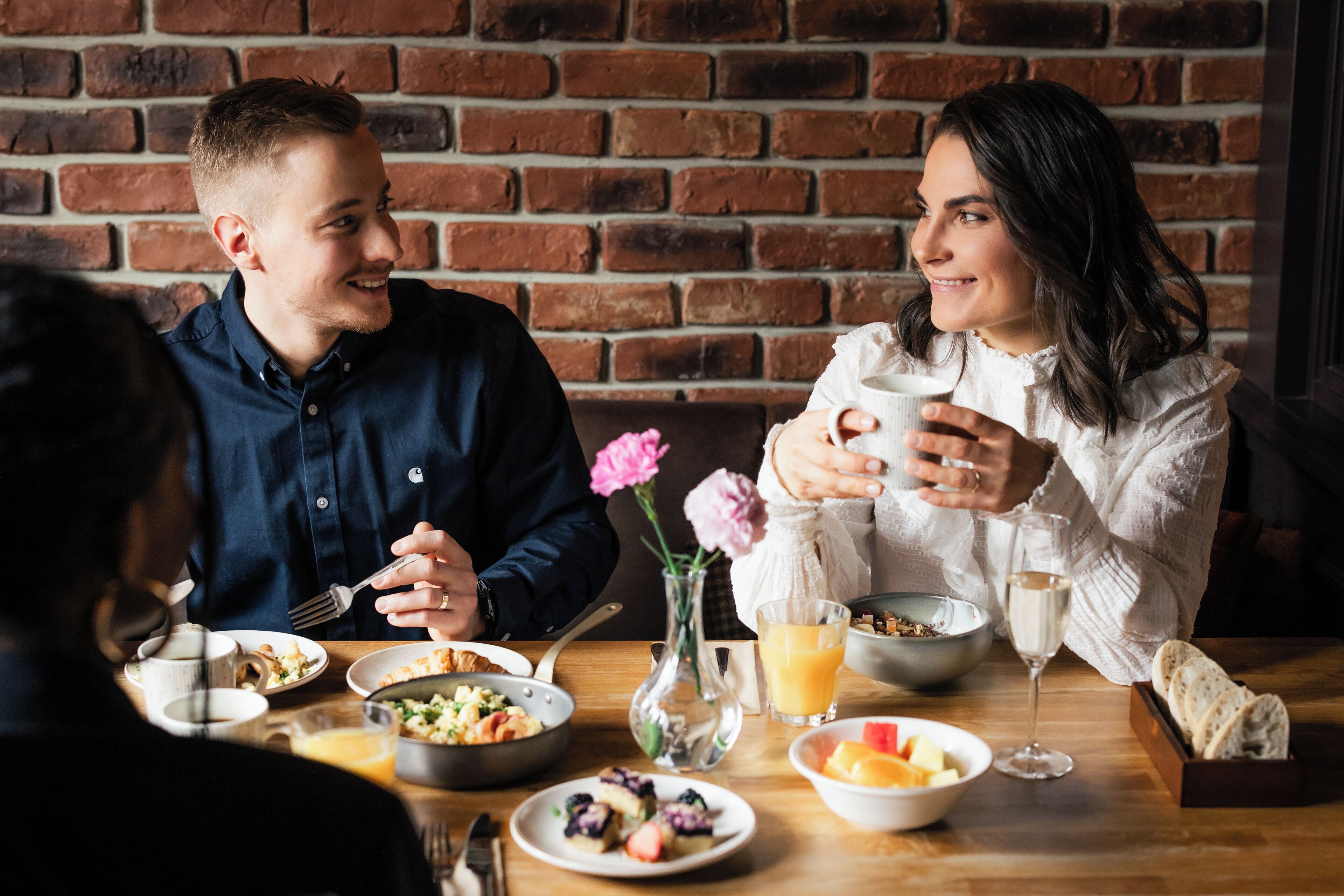 Une table à manger avec différents plats, un vase rempli de fleurs et un mur en briques en arrière-plan.