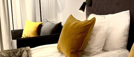 Ein Hotelzimmer mit Bett, Kissen, Decke, einer Wandlampe und einem Vorhang.