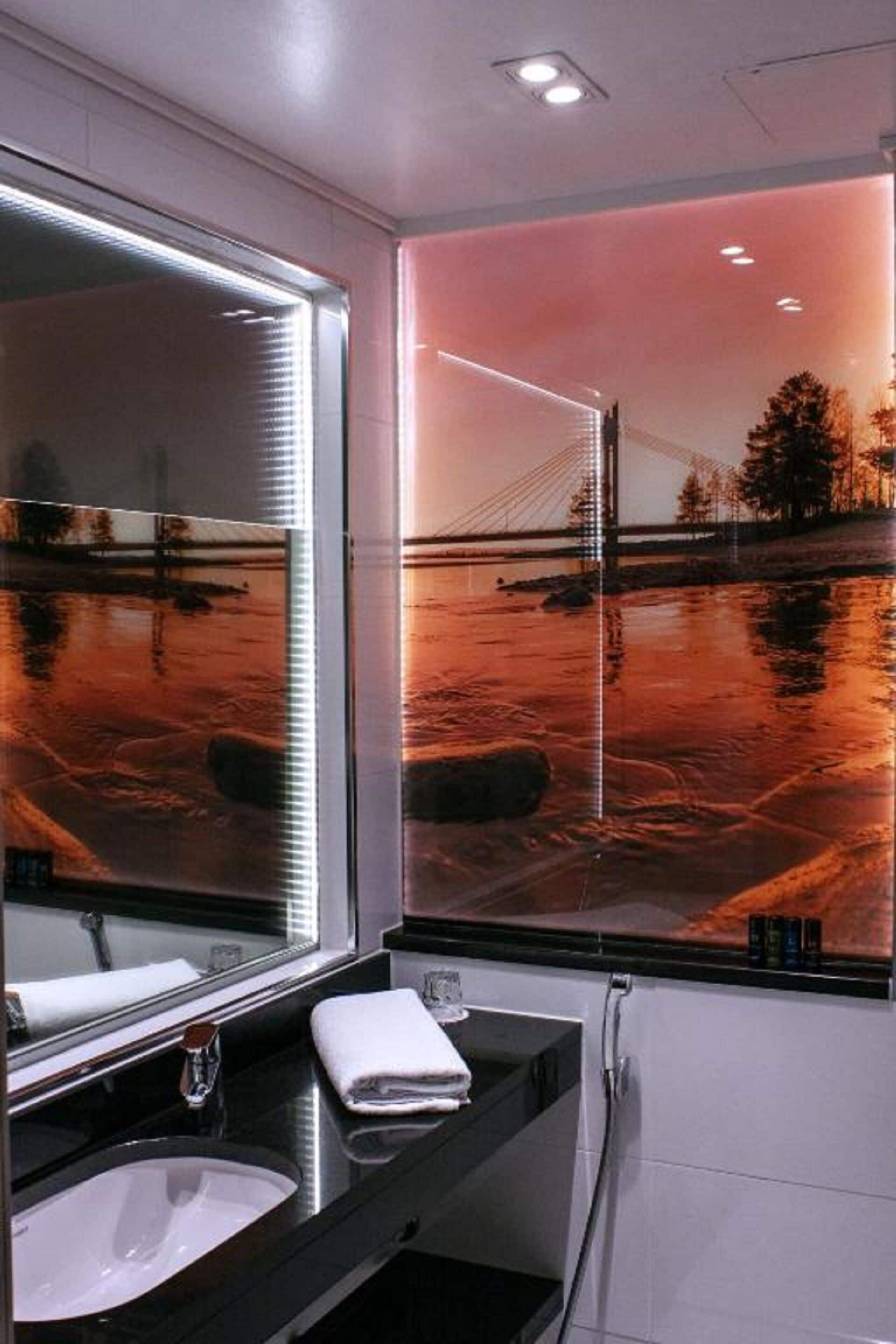 A modern bathroom with a large mirror, a sink, and a window with a view of a bridge and water.