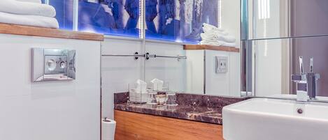 A modern bathroom with a white toilet, wooden vanity, marble countertop, and a large mirror.