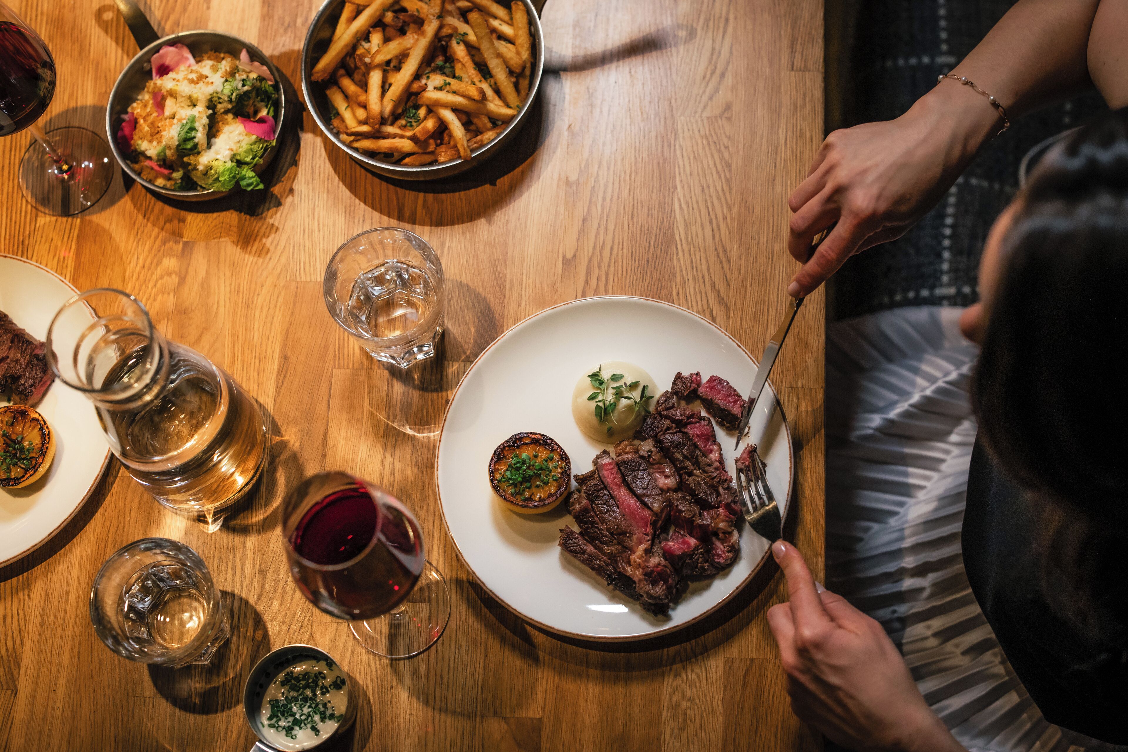 Una mesa de comedor con un bistec, papas fritas y ensalada.