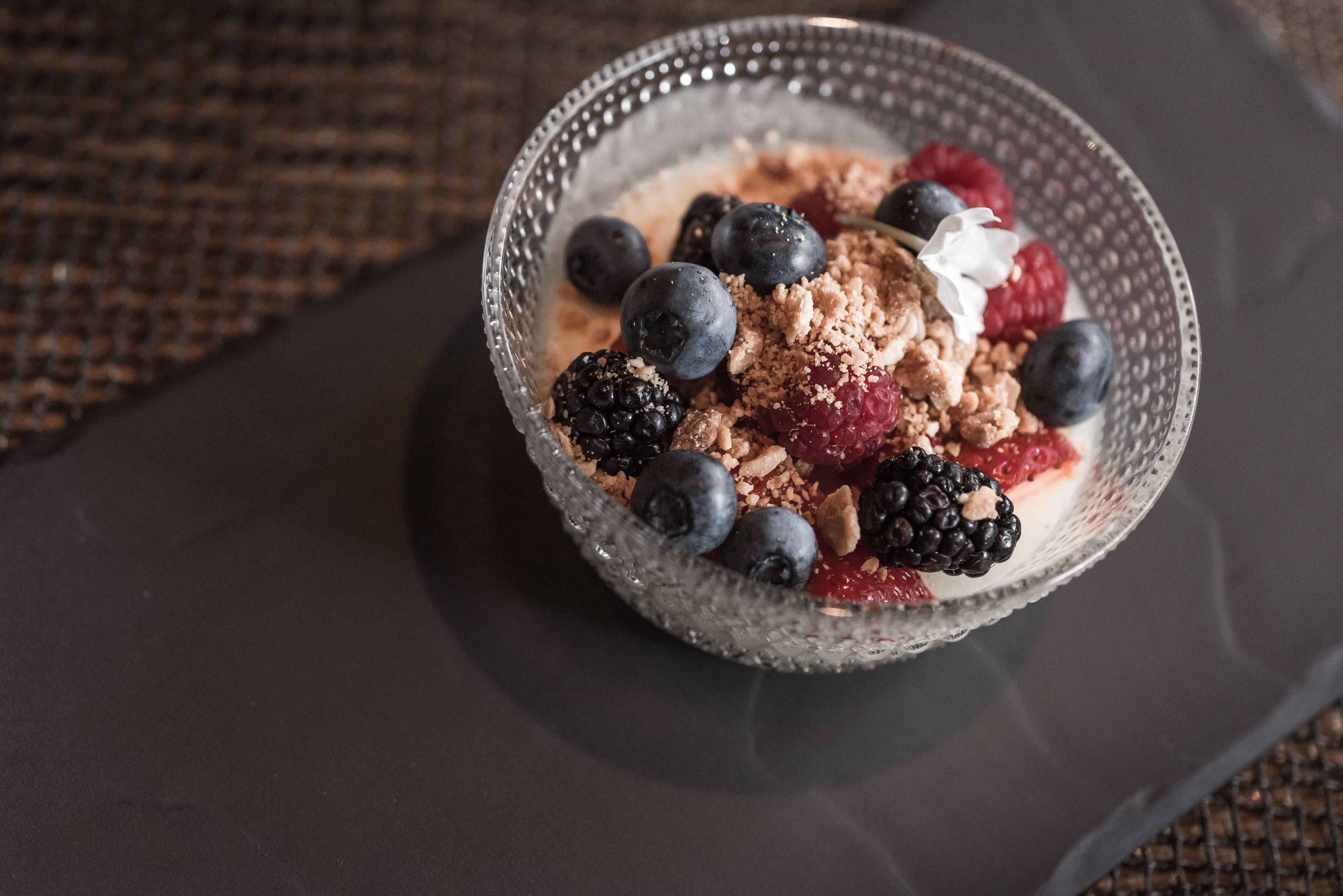A bowl of granola with blueberries, raspberries, blackberries, and a dollop of cream on a dark surface.