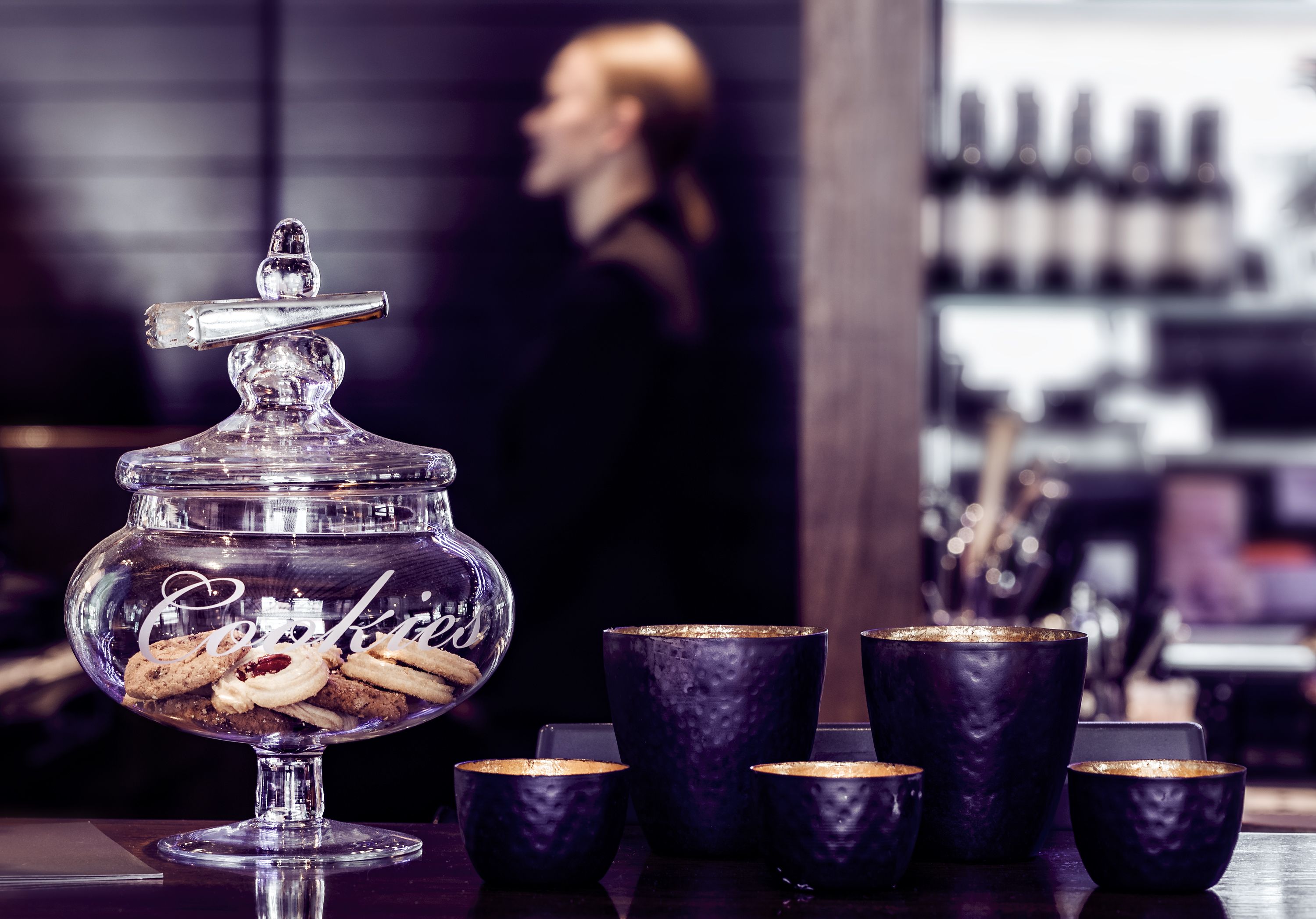Un présentoir à desserts avec un bocal en verre étiqueté « Biscuits » et plusieurs tasses foncées.