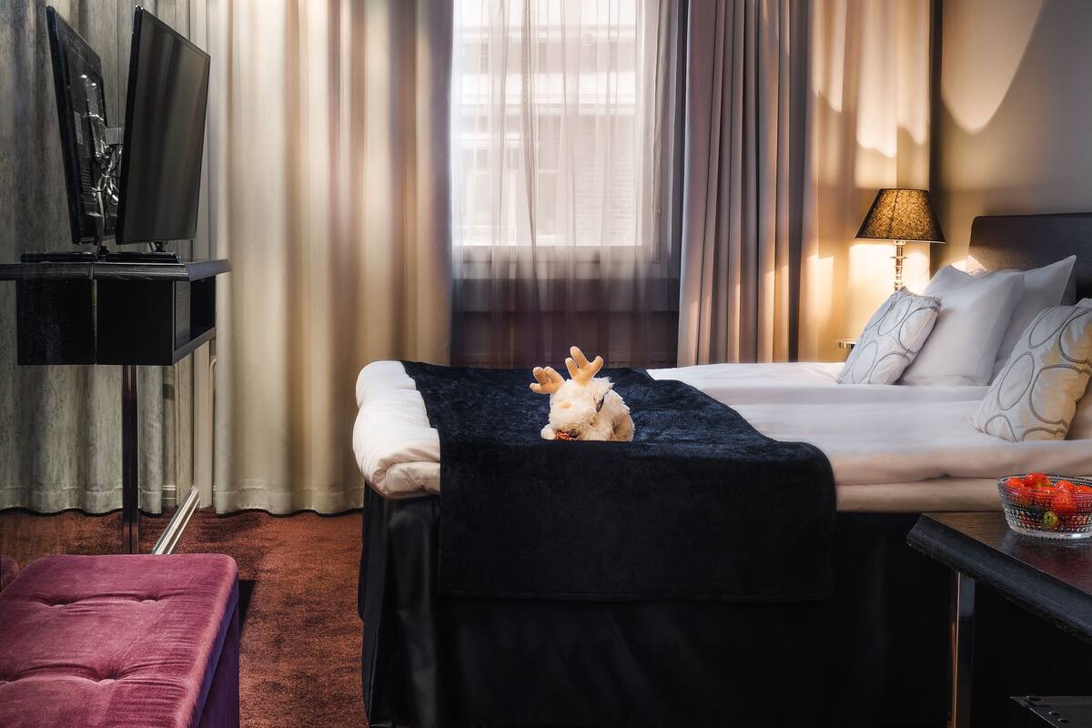 A modern hotel room with a bed, a desk, a TV, and a window with curtains.