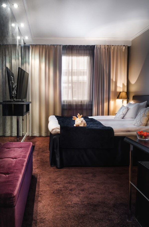 A modern hotel room with a bed, a desk, a TV, and a window with curtains.