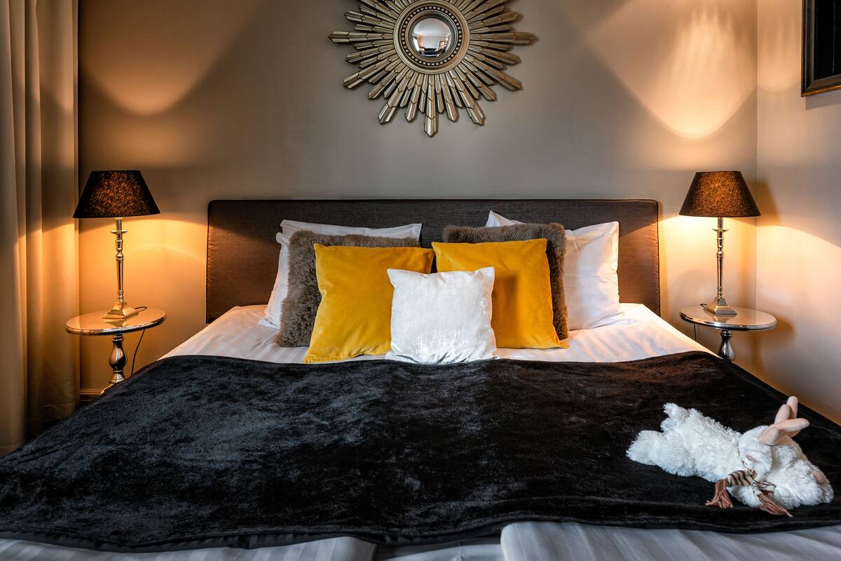 A neatly made bed with a black velvet cover, two lamps on either side, and a mirror above.