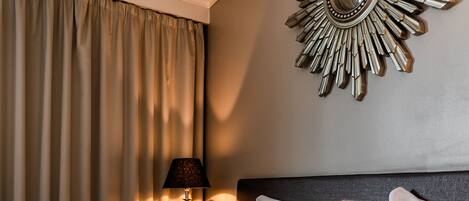A neatly made bed with a black and white duvet, a fluffy brown throw, and two yellow pillows. A decorative mirror with a sunburst design hangs on the wall above the bed.