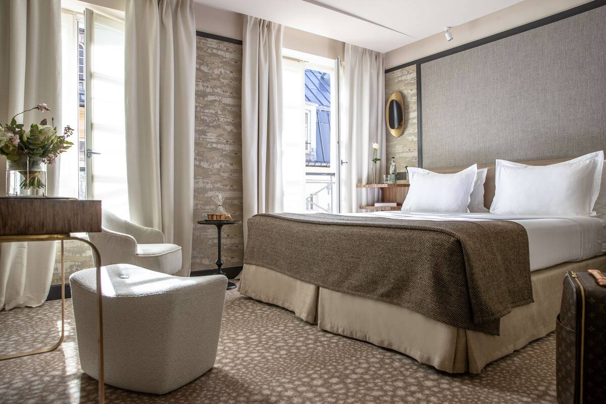 A hotel room with a bed, a chair, a desk, and a view of the outside.