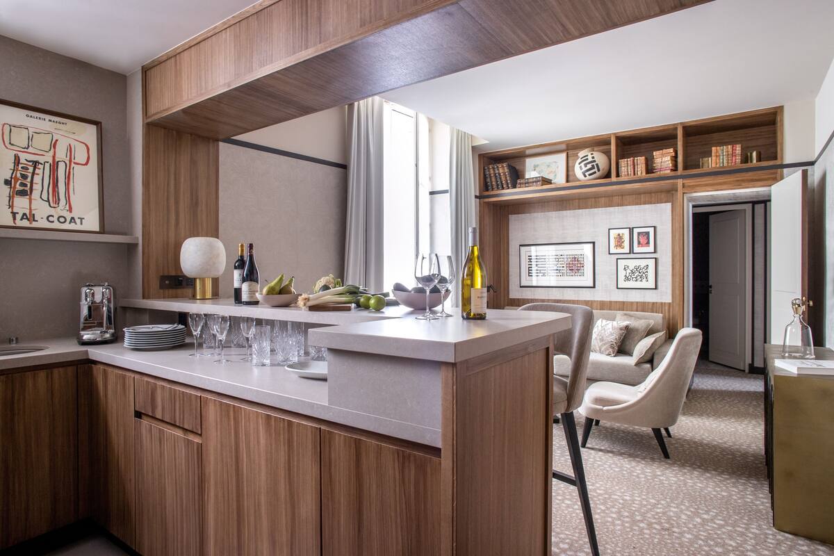A modern kitchen with wooden cabinets, a central island with glassware, and a dining area with a sofa and chairs.