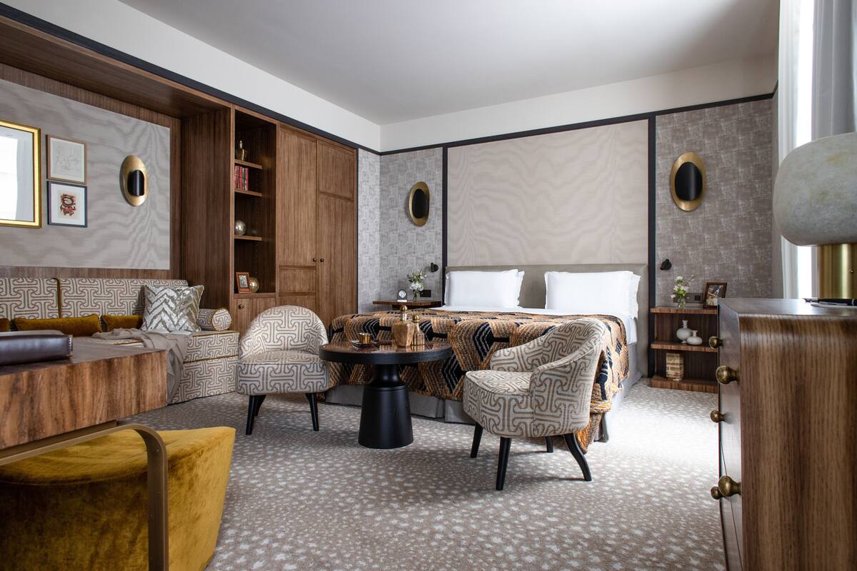 A modern hotel room with a sofa set, a dining table, and a large bed.