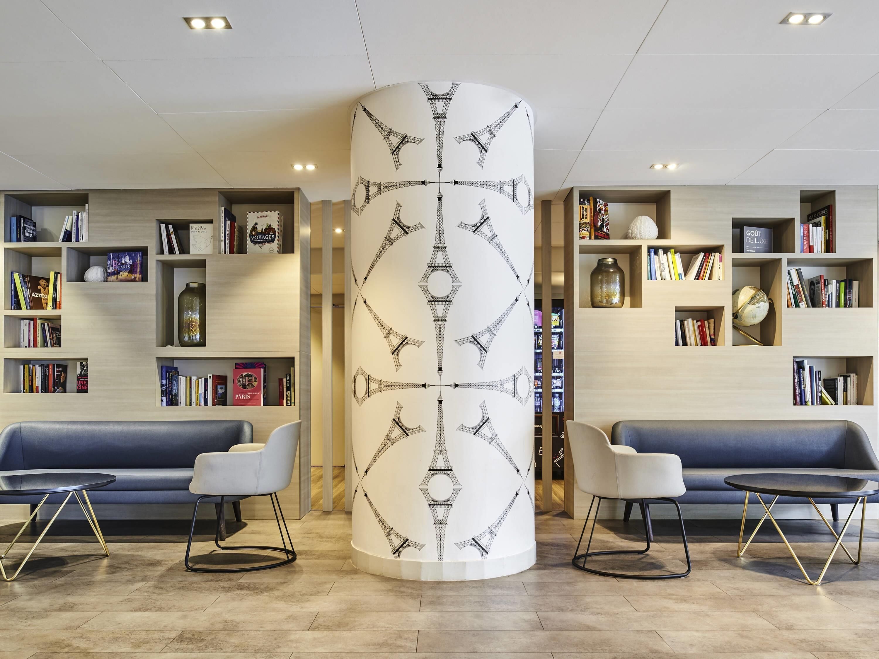 Ein modernes Interieur mit einer zentralen, zylindrischen Säule, zwei Sofas und Bücherregalen voller Bücher und Dekorationsobjekten.