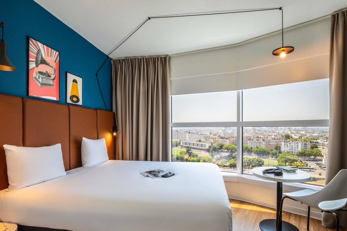 Une chambre d’hôtel moderne avec un grand lit, une vue sur la ville et une petite table avec une chaise.