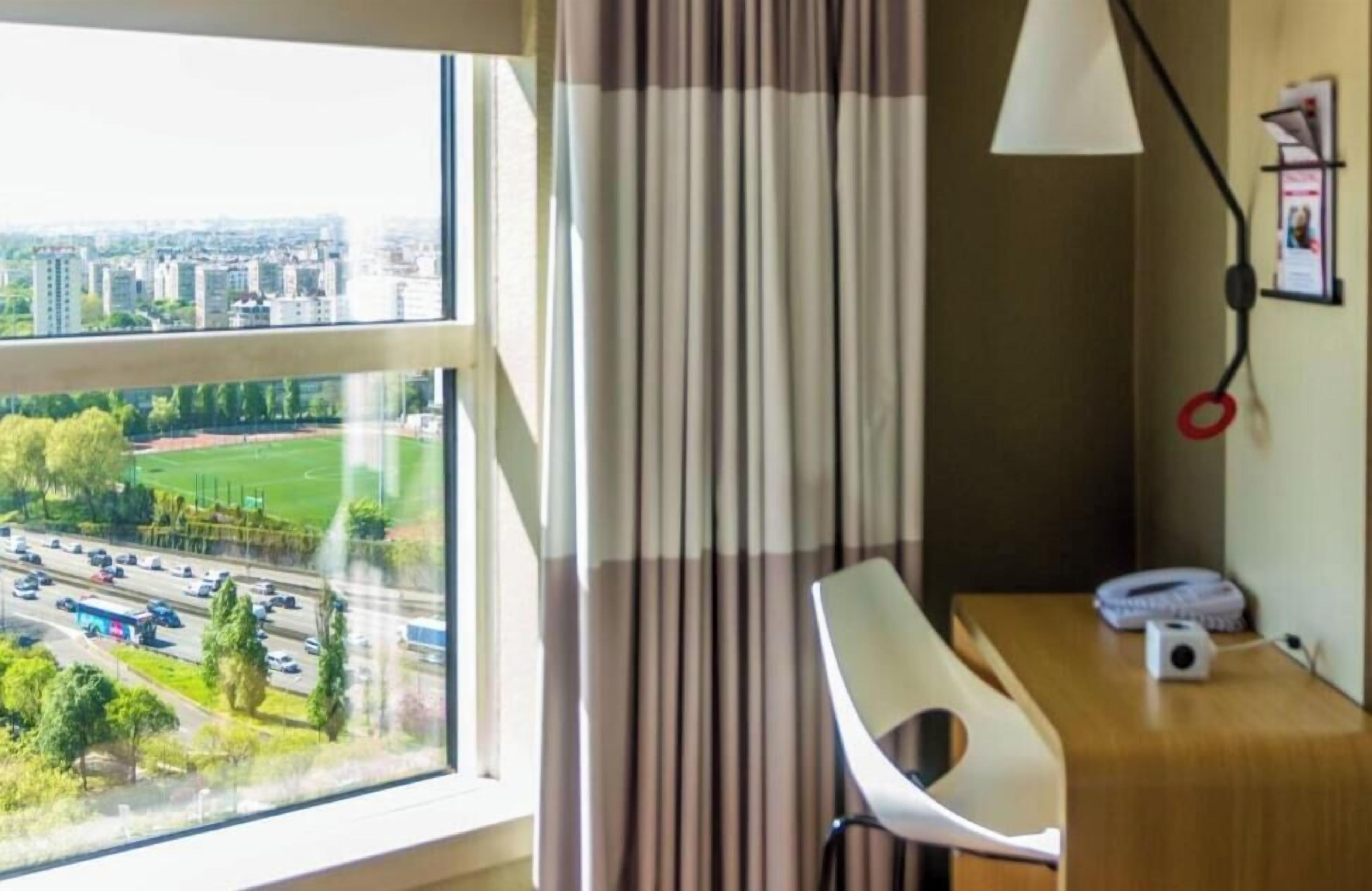 Habitació d'hotel amb una finestra gran que ofereix vista a la ciutat, un escriptori amb una làmpada i una cadira.