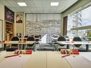 Ein Konferenzraum mit Tischen, Stühlen, einem großen Stadtbild-Wandbild, einem Bücherregal und Blick aus dem Fenster.