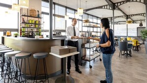 A modern bar area with a counter, stools, and a view of the city through large windows. - ibis Paris Porte De Montreuil (Paris)