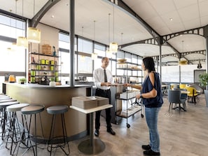 Zona de bar moderna con techos altos, amplios ventanales y diferentes tipos de asientos.