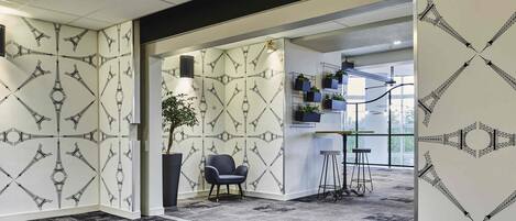 A modern office space with patterned wallpaper, a potted plant, a chair, and a bar area with stools.