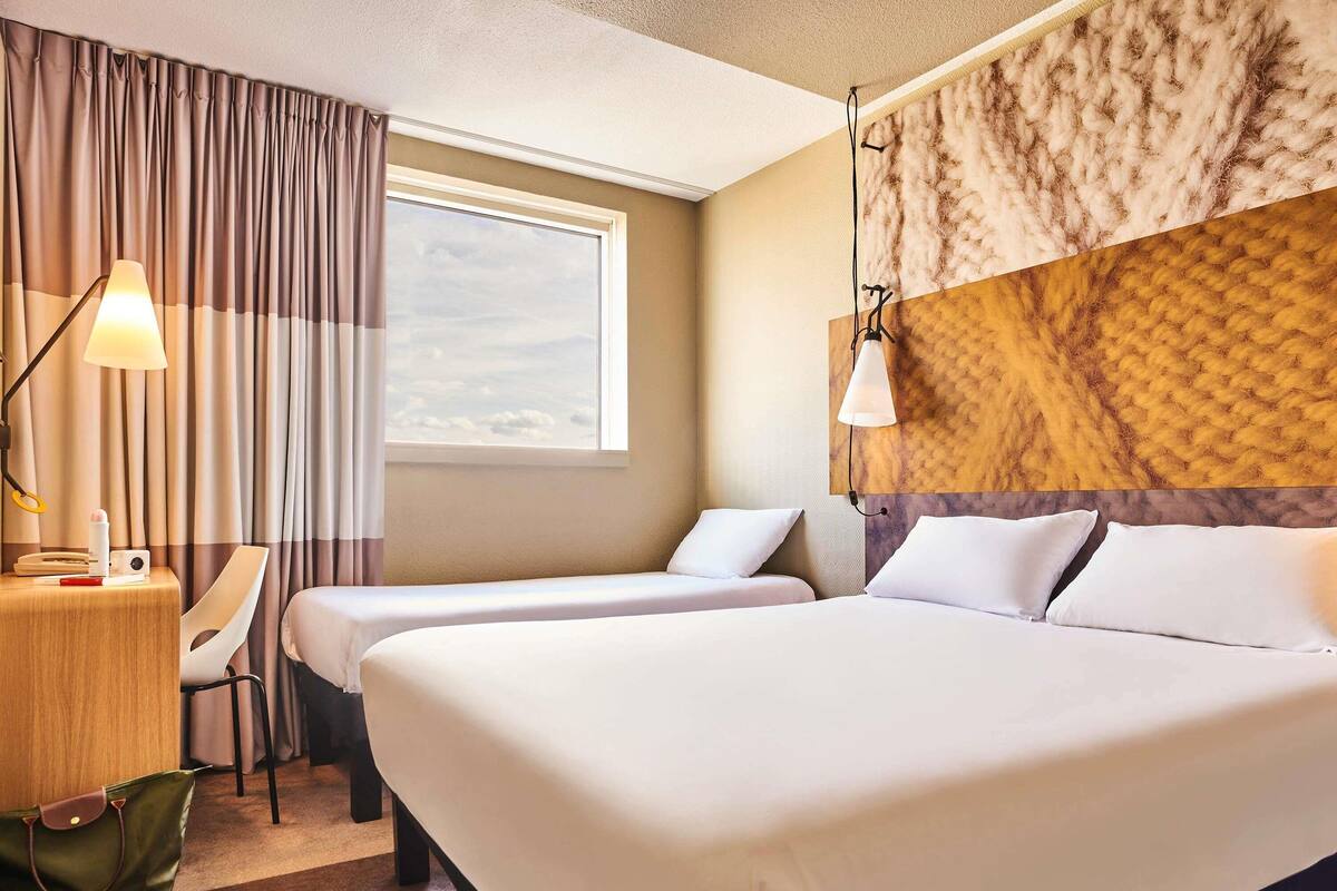 Une chambre d’hôtel avec deux lits, un bureau avec une lampe, une chaise et une vue sur le ciel par la fenêtre.