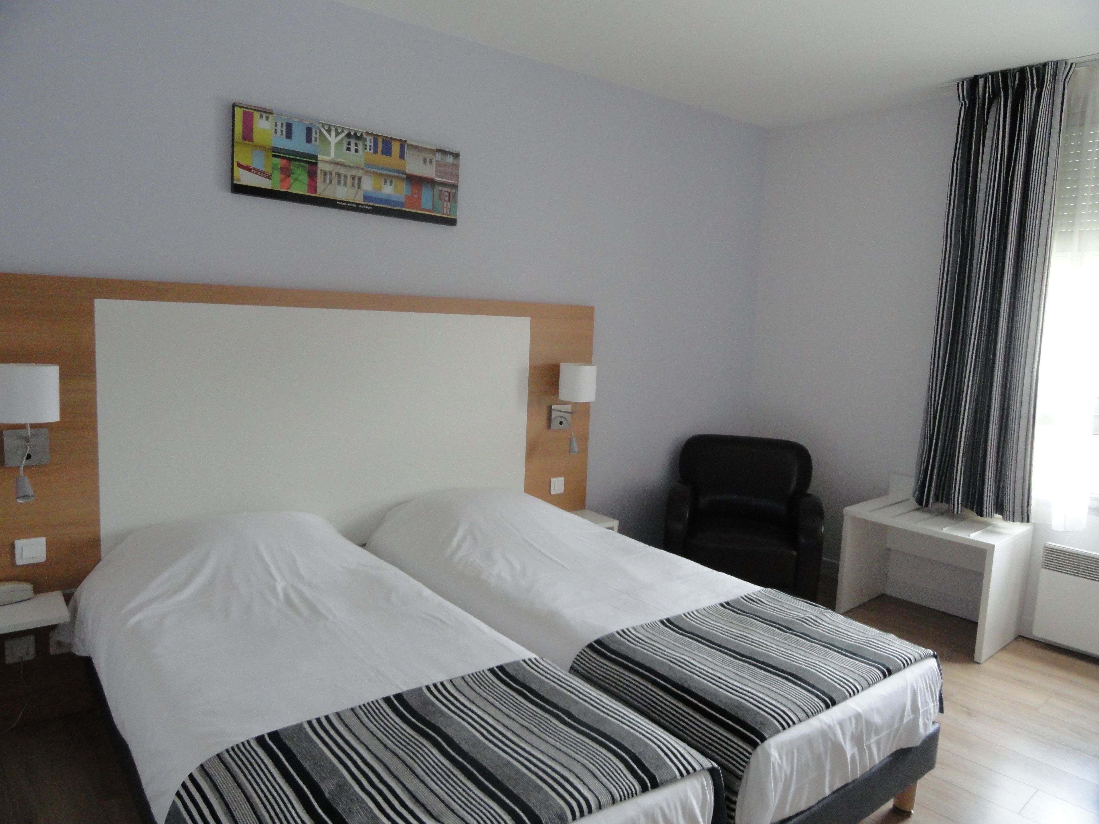 A hotel room with a large bed, a chair, a small table, and a painting on the wall.