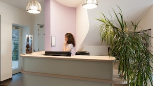 A reception area with a curved counter, a large potted plant, and a modern pendant light. - The Originals Hotels City Poitiers Continental (Poitiers)