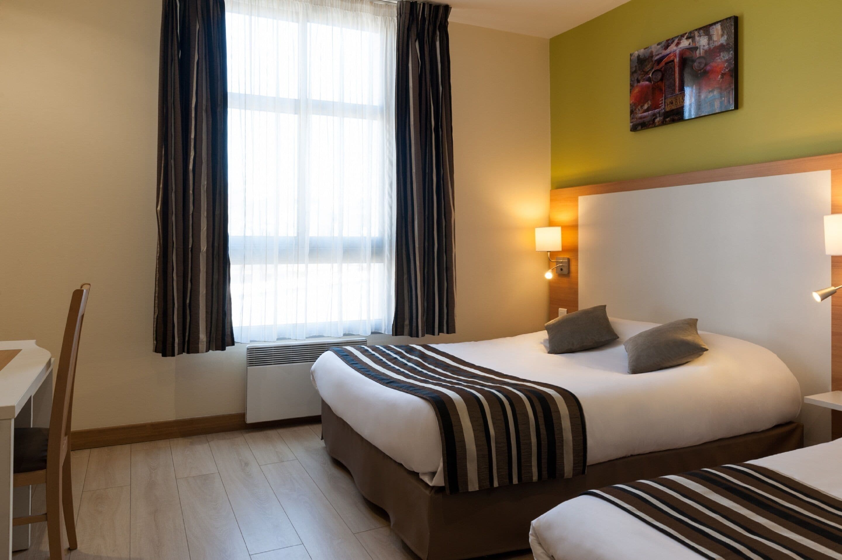 A hotel room with a bed, bedside table, lamp, and a window with curtains.