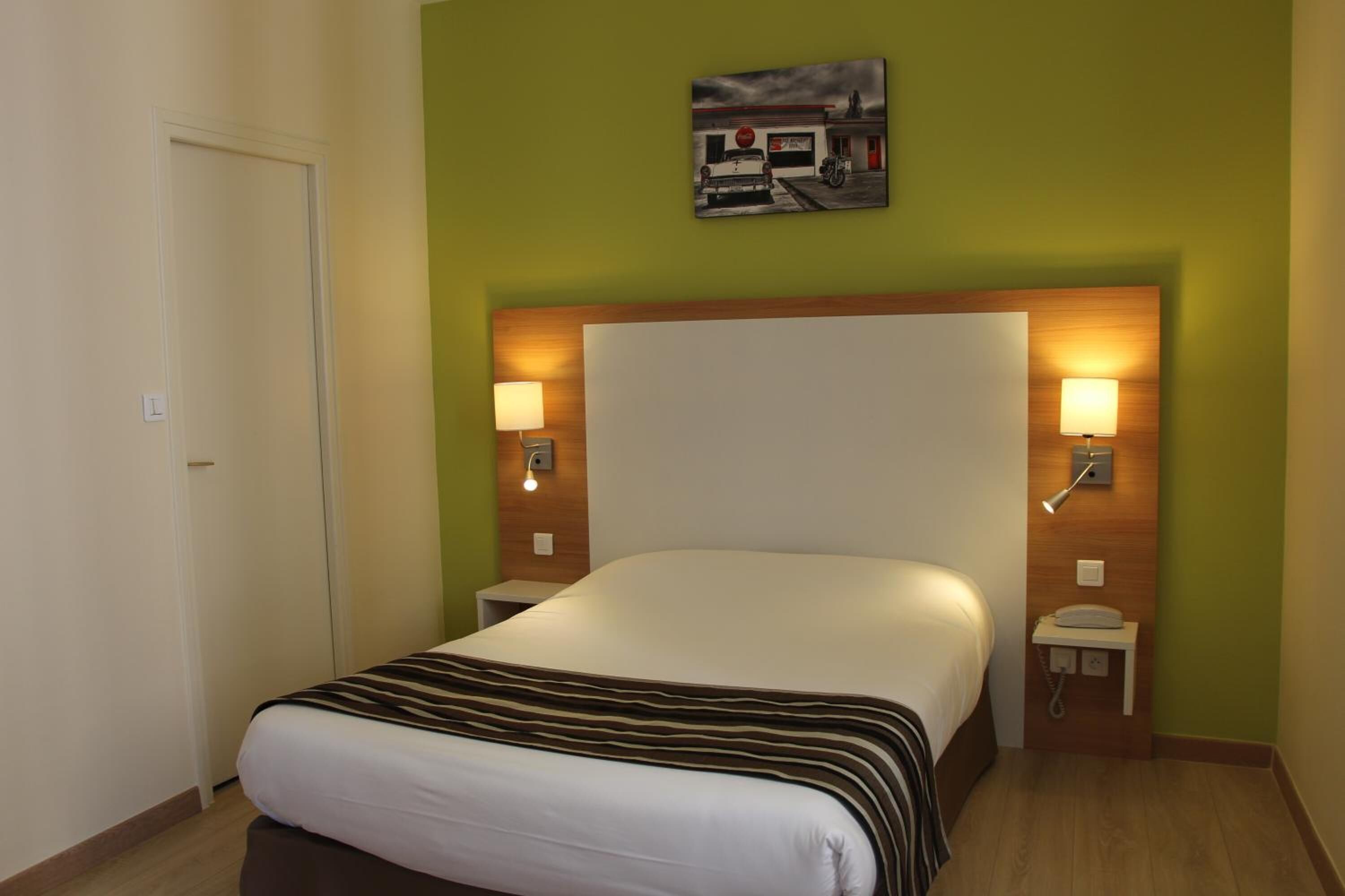 A hotel room with a large bed, two bedside tables with lamps, a wall-mounted artwork, and a door.