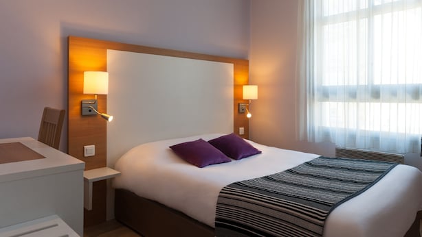 A hotel room with a large bed, two bedside lamps, a desk, and a window with sheer curtains. - The Originals Hotels City Poitiers Continental (Poitiers)
