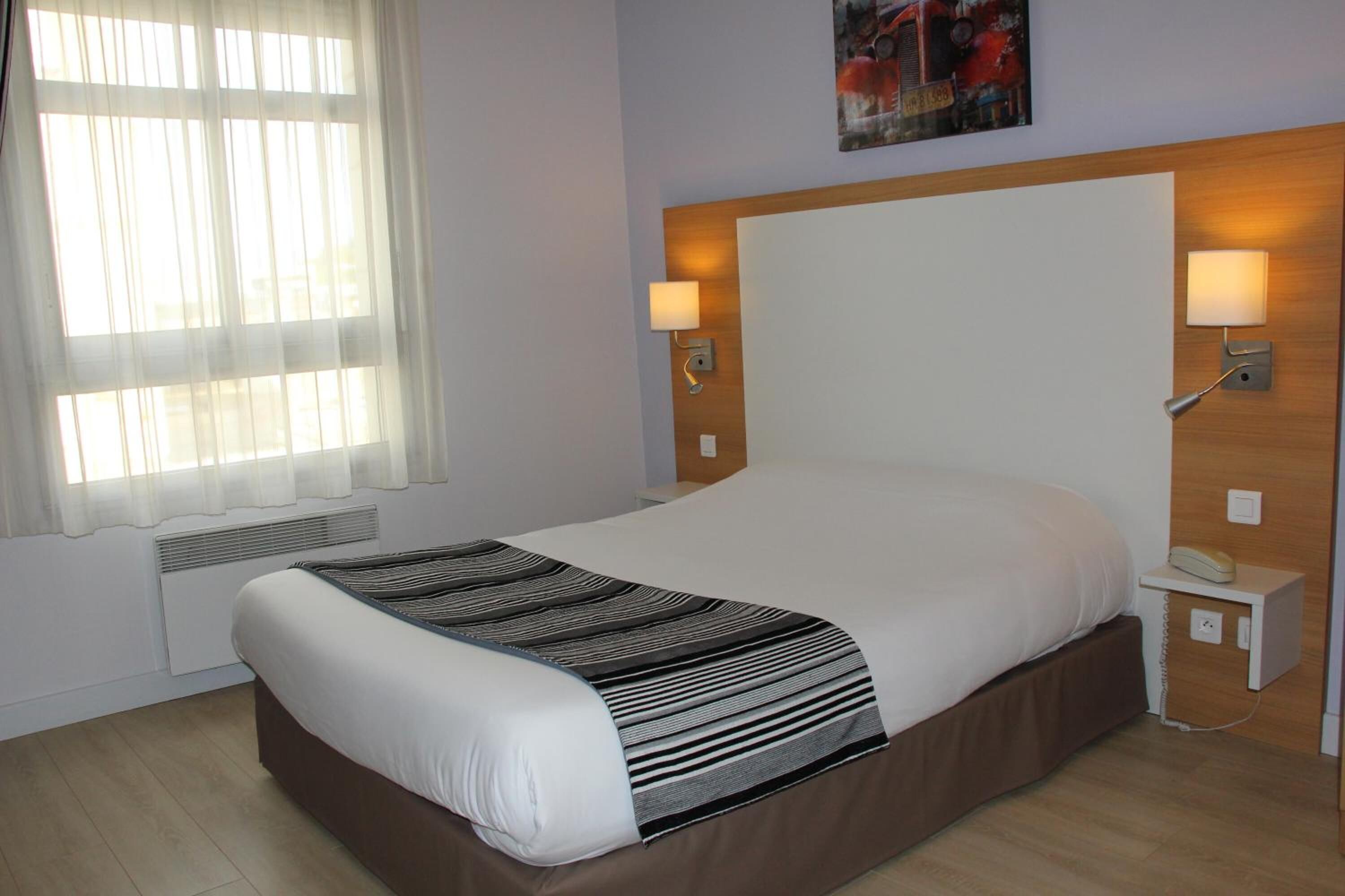 A hotel room with a large bed, two bedside lamps, a telephone, and a radiator.