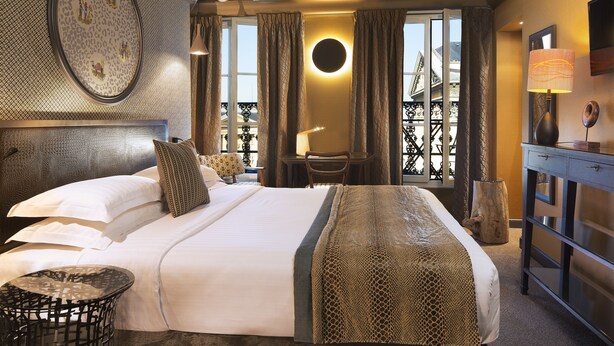 Habitación de hotel con una cama grande, un espejo redondo, un escritorio y vistas al balcón exterior.