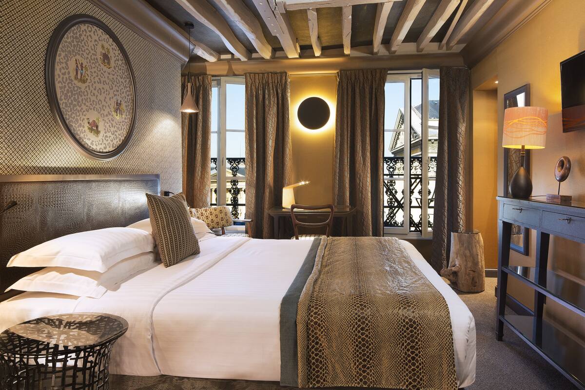 A hotel room with a large bed, a round mirror, a desk, and a view of the outside balcony.