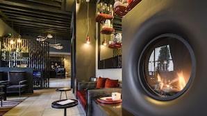 Un área de descanso moderna con chimenea, asientos y un bar con botellas y vasos.