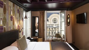 Habitación de hotel con cama, una silla, televisor y balcón con vistas.